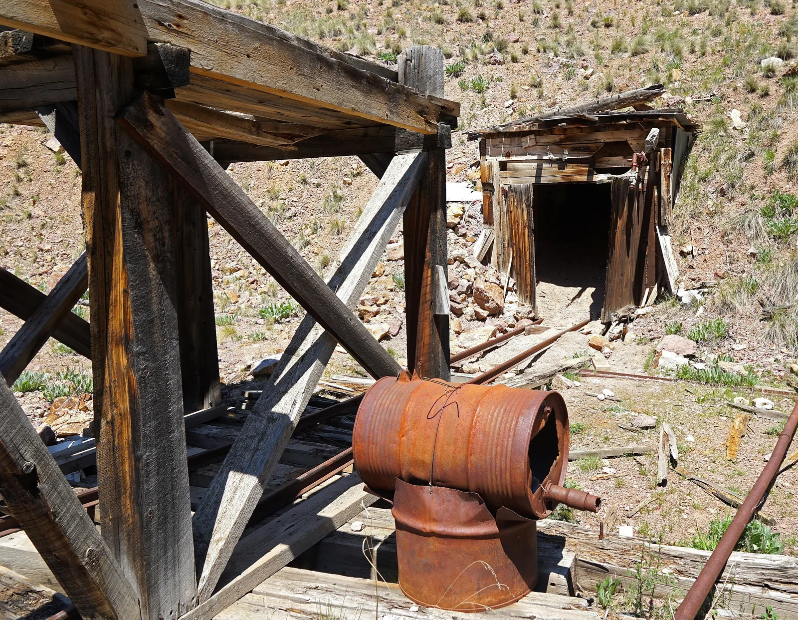 A weathered timber mine adit entrance partially collapsed on a hillside, with a faded BLM warning sign posted beside the opening